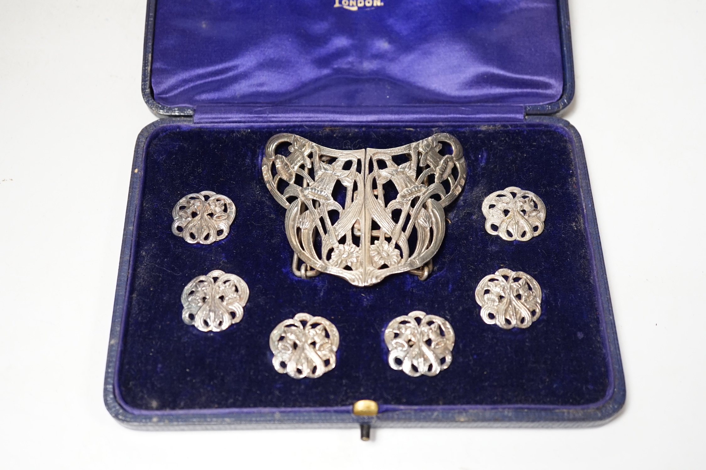 An Edwardian cased silver buckle and button set comprising a buckle and six buttons, Samuel Jacob, London, 1908, buckle width 76mm.